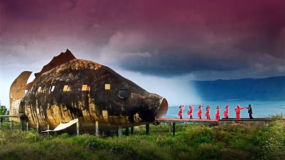 A line of figures in red stands beside a giant fish-shaped building under stormy skies