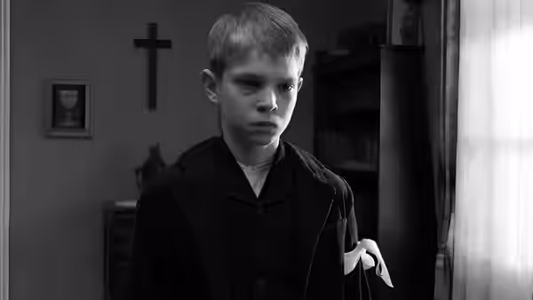 a young boy standing in a room with a cross on the wall