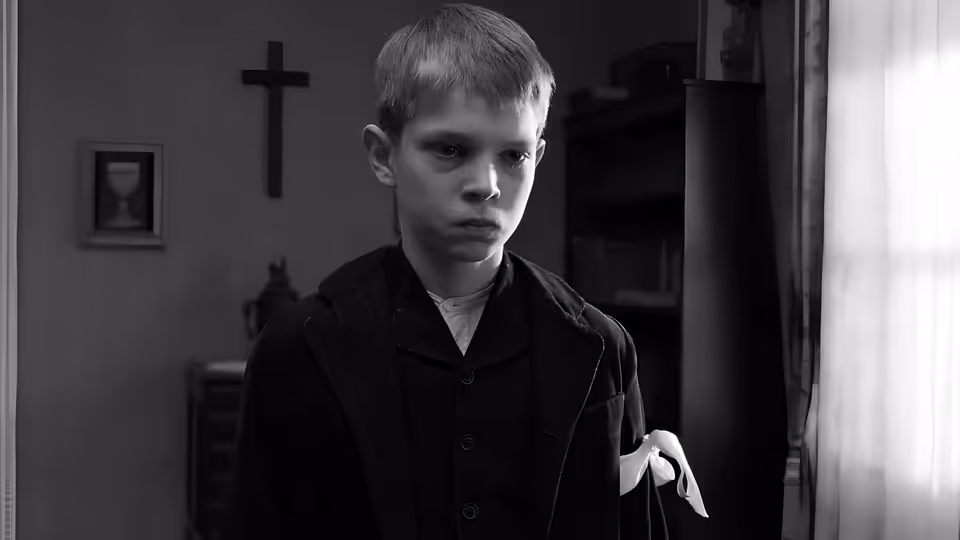 a young boy standing in a room with a cross on the wall