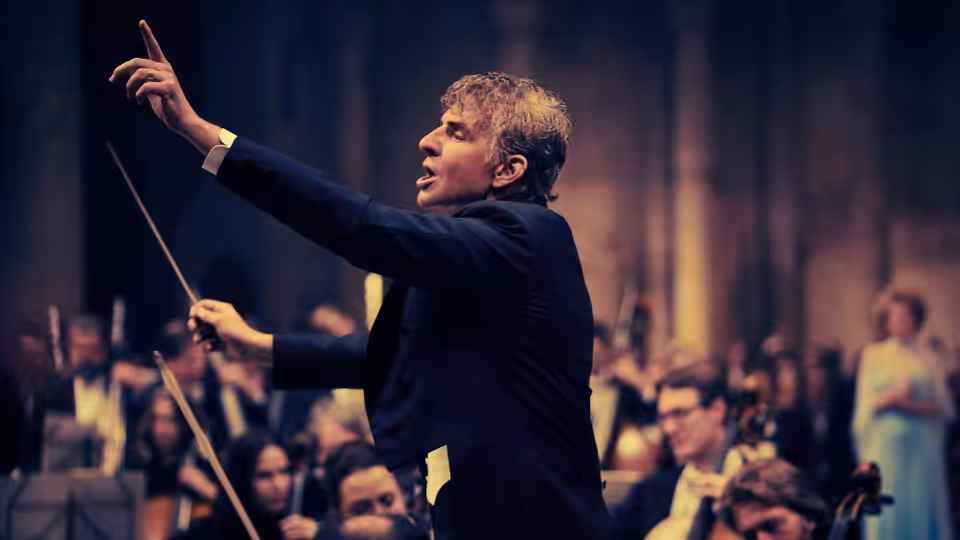 Leonard Bernstein (Bradley Cooper) conducting an orchestra with baton raised