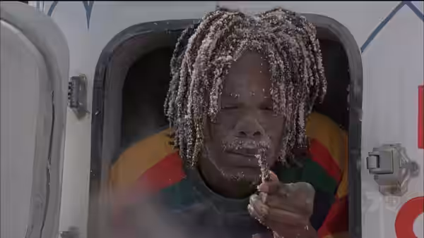 A dreadlocked bobsledder blows frost from his fingers inside the sled