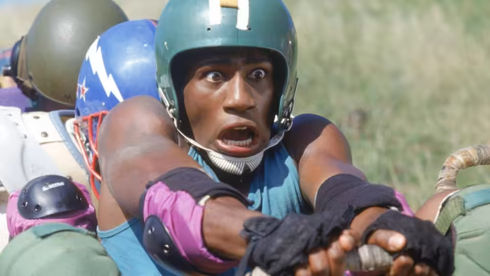 A bobsledder in a green helmet braces at the front of a training sled