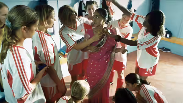 Footballers gather around a woman in a pink sari in the changing room