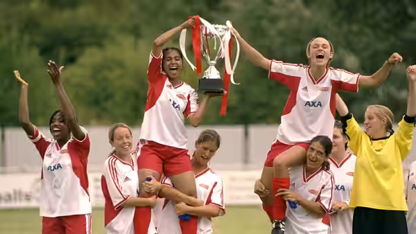 Jess (Parminder Nagra) and Jules (Keira Knightley) celebrate with their teammates, raising a trophy on the football field