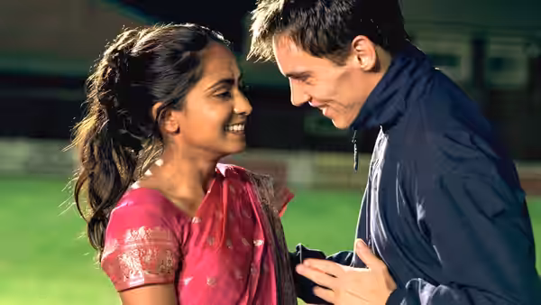 Jess (Parminder Nagra) smiles at Joe (Jonathan Rhys Meyers) beside the football pitch