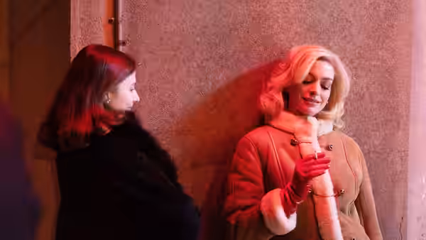 Rebecca (Anne Hathaway) leaning against a wall next to Eileen (Thomasin McKenzie)