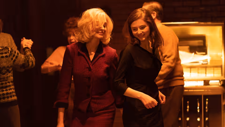Rebecca (Anne Hathaway) and Eileen (Thomasin McKenzie) walking together through a bar