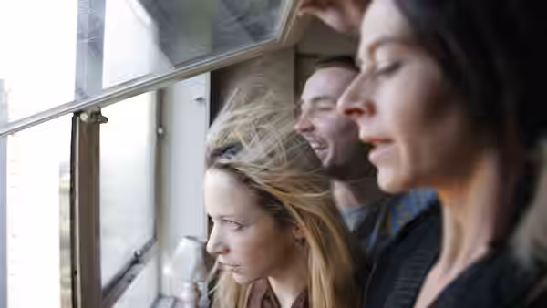 Two women and a man peer through an open window