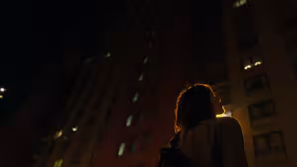 A woman looks up at a high-rise apartment building at night