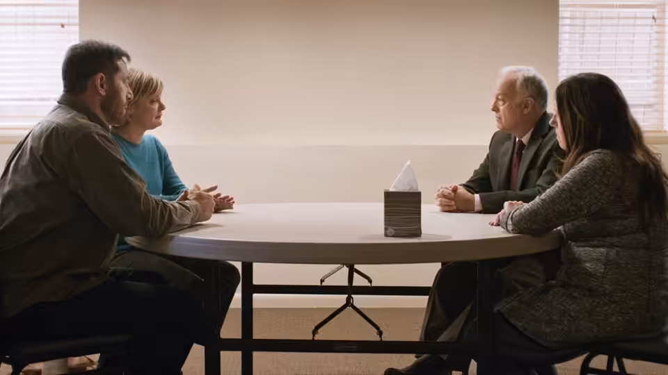 Jay (Jason Isaacs) and Gail (Martha Plimpton) face Richard (Reed Birney) and Linda (Ann Dowd) across a meeting-room table
