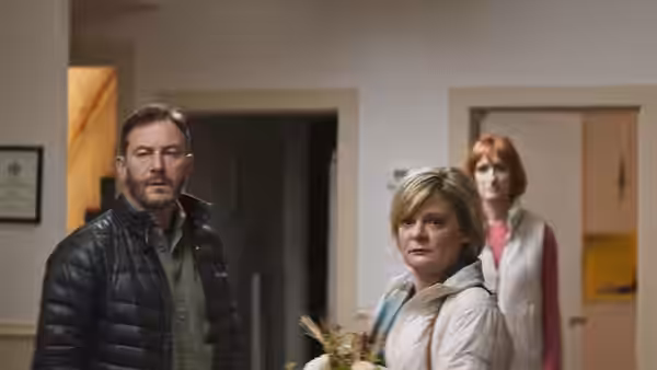 Jay (Jason Isaacs) and Gail (Martha Plimpton) enter a room as a red-haired woman stands behind them