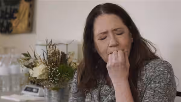 Linda (Ann Dowd) sits beside a bouquet, pressing her fingers to her lips