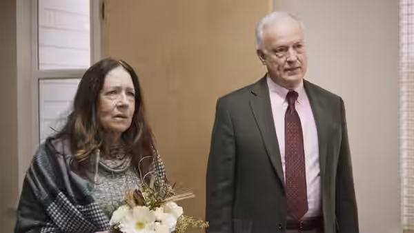 Linda (Ann Dowd) holds a bouquet beside Richard (Reed Birney) in a meeting room