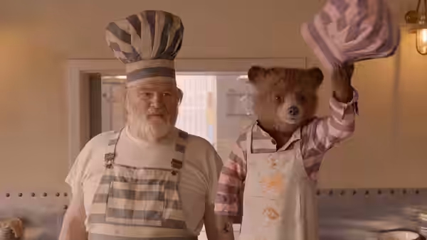 Knuckles McGinty (Brendan Gleeson) watches as Paddington raises a chef hat