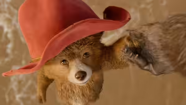 Paddington in a red hat is grabbed by a fox-like paw