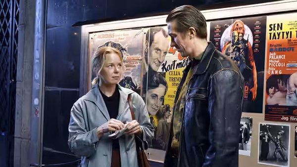 Ansa holding a ticket beside Holappa in front of movie posters