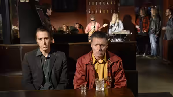 Holappa and another man seated at a bar table with a band behind