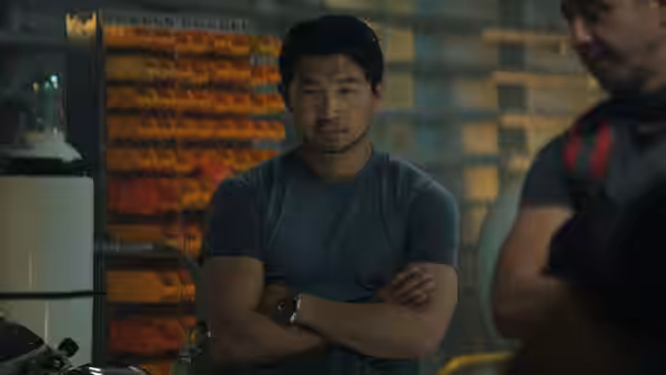 Simu Liu as David Yuasa standing with arms crossed in a workshop