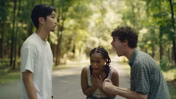 Day (Akira Jackson) stands between two young men on a forest road