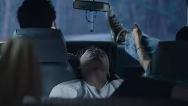 A young man reclines with feet up inside a moving vehicle