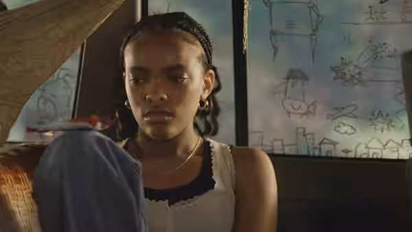 Day (Akira Jackson) sits inside holding blue fabric and looking ahead