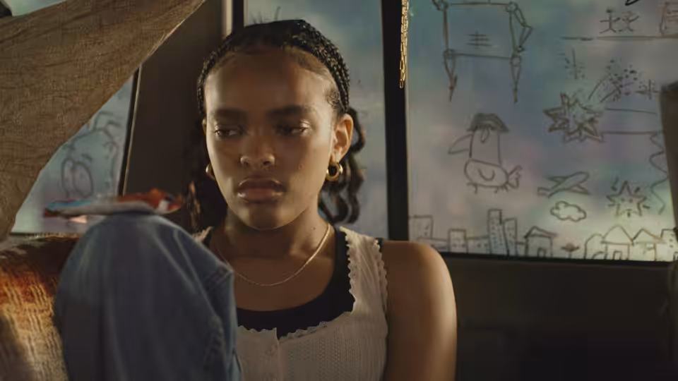 Day (Akira Jackson) sits inside holding blue fabric and looking ahead