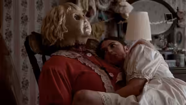 Dolly sits with a woman in a white dress in a bedroom