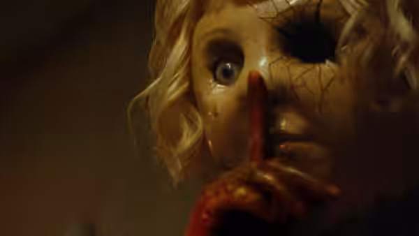 Close-up of Dolly's cracked doll mask with finger to lips