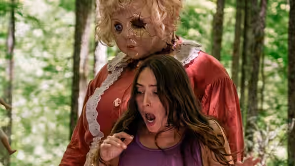 Dolly stands behind a terrified woman in a forest