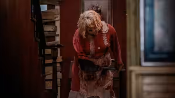Dolly holds a chainsaw while standing inside a house