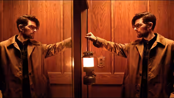 Ohm Bauman (Adam Scott) holding a lantern beside a mirror in a wooden room