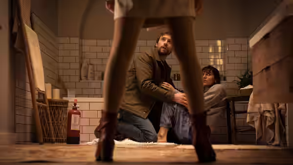 A man kneels on the bathroom floor beside a seated woman viewed between standing legs