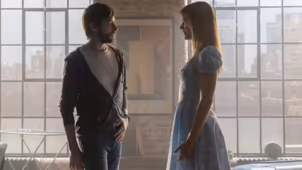 A bearded man and a woman in blue face each other in a sunlit loft