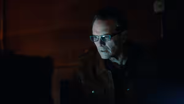 an older man with glasses looking to the side in darkness