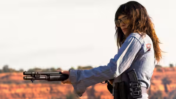 a woman in sunglasses aiming a shotgun across a desert landscape