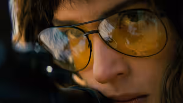 a woman in yellow-tinted glasses aiming a firearm at close range