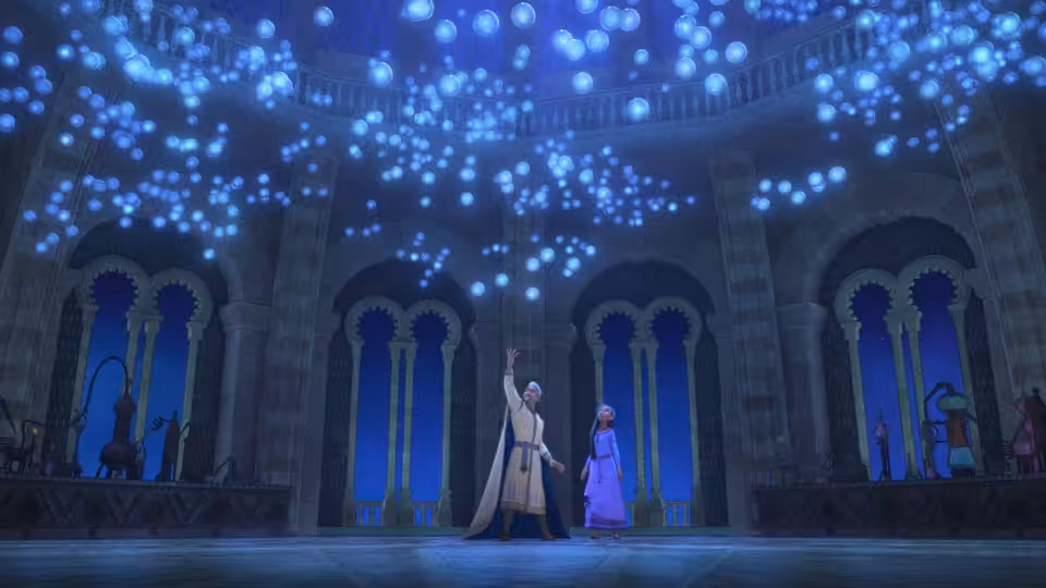 King Magnifico (Chris Pine) and Queen Amaya (Angelique Cabral) stand in a grand hall under floating orbs