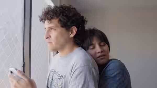 Jaime (Luciano Reinoso) holds his phone by the window as Camila rests on his shoulder