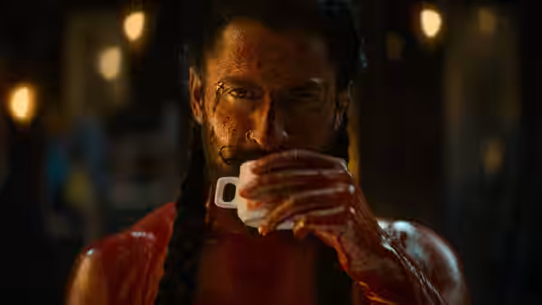 Man with braided hair covered in red liquid drinks from a white cup