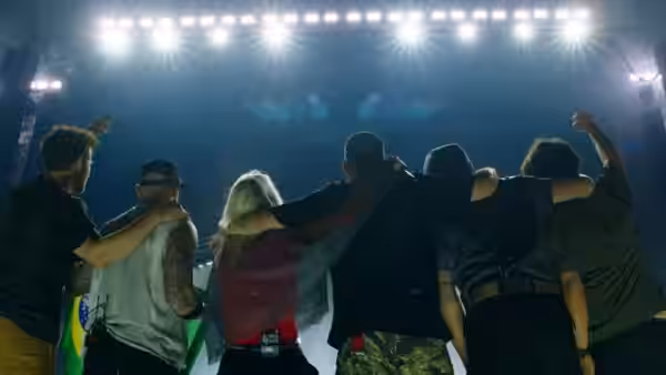 Band members stand arm in arm facing the audience beneath bright stage lights