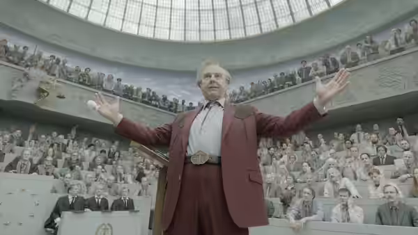 President Compson (John Goodman) standing at the podium with arms outstretched