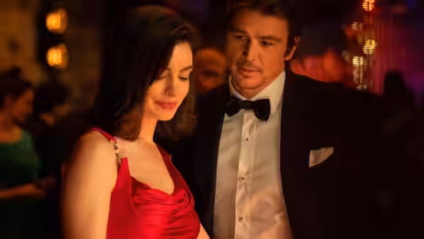 Verity Crawford (Anne Hathaway) in a red dress standing beside Jeremy Crawford at a party