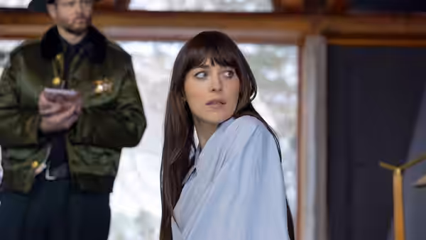 Lowen Ashleigh (Dakota Johnson) in a white robe looks back as a man stands behind her