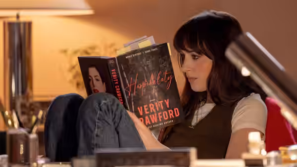 Lowen Ashleigh (Dakota Johnson) reading Verity Crawford's book while reclining on a sofa