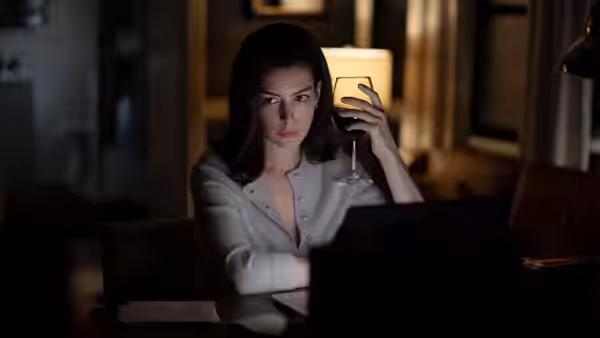 Lowen Ashleigh (Dakota Johnson) holds a glass while seated at a laptop indoors