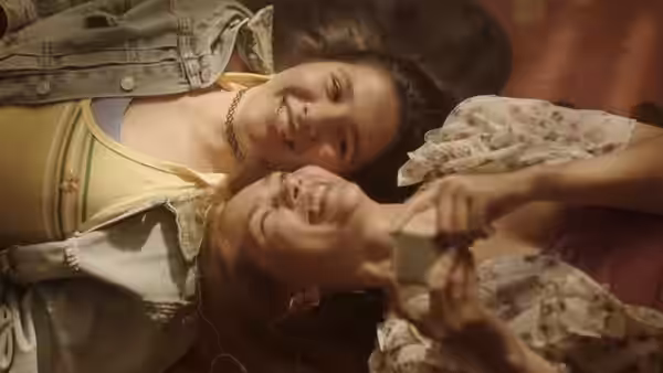 Two smiling women lie on their backs taking a selfie together with a camera