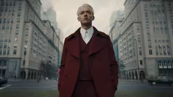 Coriolanus Snow (Tom Blyth) standing in a city street wearing a red coat