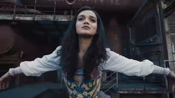 Lucy Gray Baird (Rachel Zegler) with arms extended standing in an industrial setting