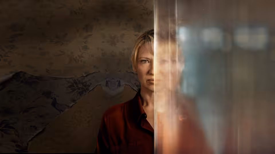 A woman peers through a glass partition, her face partly hidden behind its frame