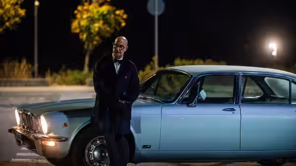 Roger (Stanley Tucci) leans against a vintage sedan at night